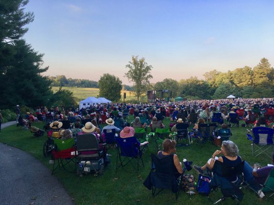 people seated in chairs on a lawn listening to music on a stage